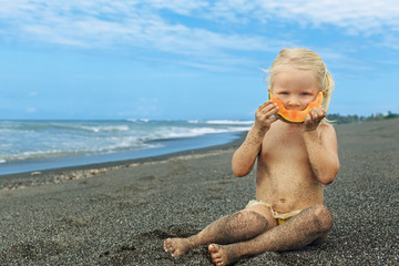 Little cute girl on the sea beach eating ripe papaya