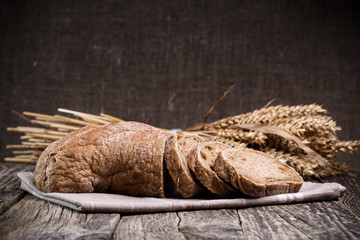 Tasty bread with wheat on wooden background.