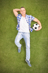 Casual man lying on a field and holding football