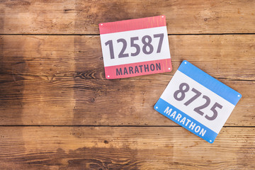 Two marathon race numbers laid on a wooden floor background