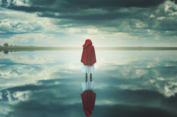 Red hooded woman in a strange landscape with clouds