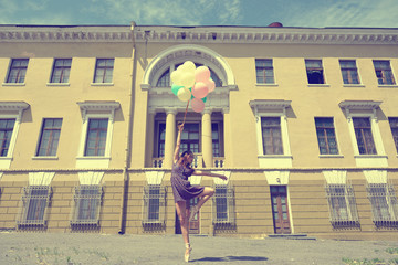 Attractive teen girl dancing with ballons outdoor against old bu