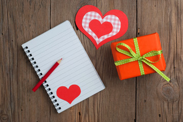 Notebook with gift, pencil and hearts on old wooden background