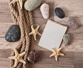 Fototapeta na wymiar paper, rope, starfish, sea stones on the old wooden background