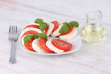 Tomato and mozzarella with basil leaves on a white plate