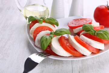 Tomato and mozzarella with basil leaves on a white plate