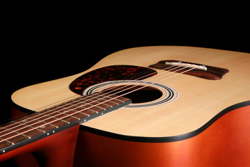 Close up of an acoustic guitar set against a black background