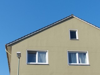Wohnhaus mit Spitzgiebel und Fassade in Beige und Naturfarben vor blauem Himmel bei Sonnenschein in...