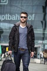 Fototapeta na wymiar Attraktiver Mann mit Sonnenbrille und Reisetasche