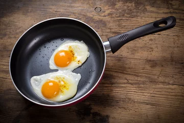 Fotobehang Spiegeleieren frying eggs in pan on table