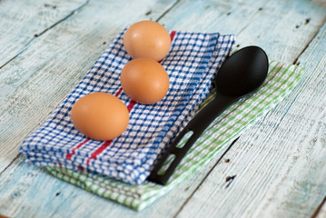 Eggs with spoon and dish towel on old wooden table