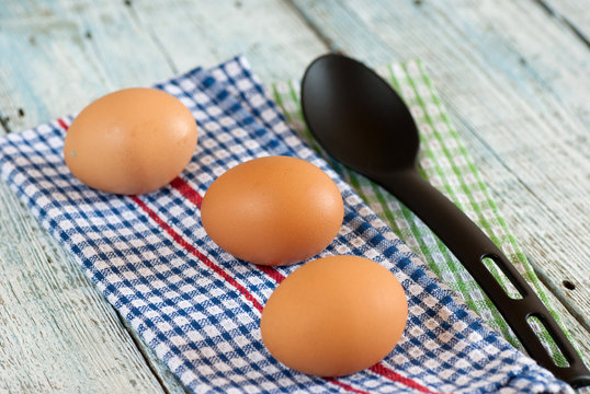 Eggs with spoon and dish towel on old wooden table