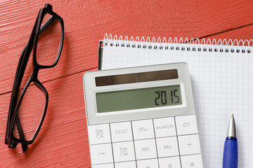 Calculator with 2015 sign, notepad, pen and glasses