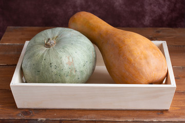 Two different pumpkins on a wooden tray.