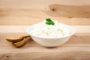 Fresh cottage cheese in a white bowl on a wooden table.