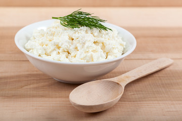 Fresh cottage cheese in a white bowl with spoon on a wooden.