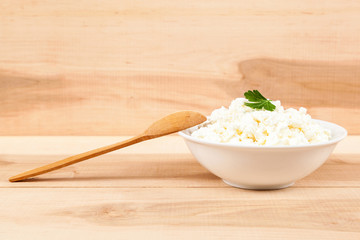 Fresh cottage cheese in a white bowl with spoon on a wooden.