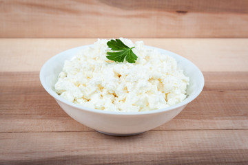 Fresh cottage cheese in a white bowl on a wooden table.
