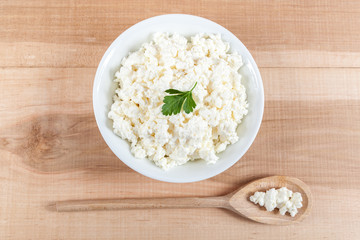 Fresh cottage cheese in a white bowl with spoon on a wooden.