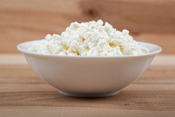 Fresh cottage cheese in a white bowl on a wooden table.