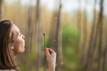 Young woman in the park holding blowing dandelion flower seed