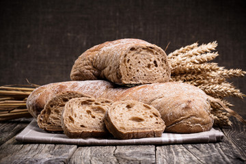 Tasty bread with wheat on wooden background.