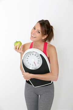 Cheerful girl in fitness outfit holding scale and green apple