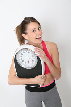 Cheerful girl in fitness holding scale, isolated