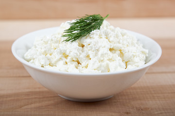 Fresh cottage cheese in a white bowl on a wooden board.