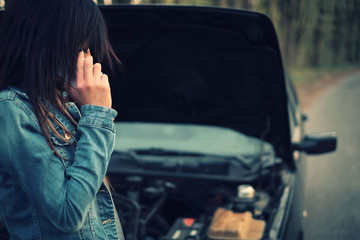 Woman with brown hair under the hood of her car break down