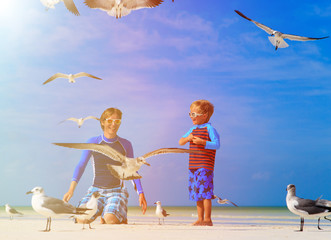 father and son feeding seagulls on the beach