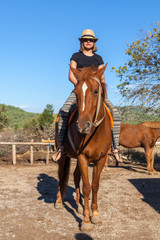 Girl in hat riding on a brown horse