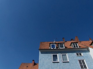 Altbau mit Mansarden, Dachgaube und hellblauer Fassade vor blauem Himmel im Sonnenschein im...