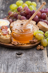 flavored honey, bread and butter and grapes on wooden background