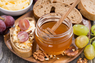 flavored honey, bread with butter and grape on wooden board