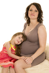 mother in brown dress and daughter laying on pregnant belly