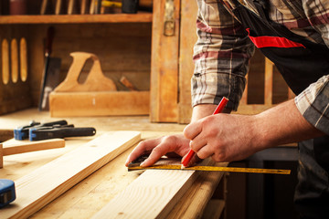 Carpenter marking a measurement on a wooden plank - obrazy, fototapety, plakaty
