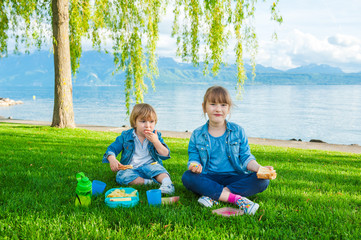 Two cute kids having a picnic outdoors by the lake