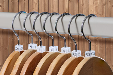 Wooden hangers with indexes of the sizes on wooden background.