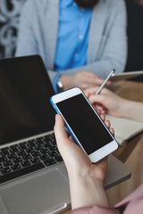 Woman with smartphone taking notes over laptop in cafe