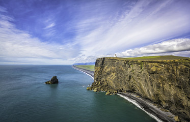 Fototapeta na wymiar The black sand beach with Lighthouse on the cliff