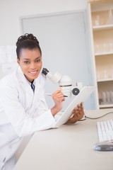 Smiling scientist looking at camera and taking notes