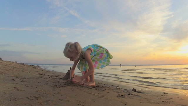 The little girl plays with sand on a beach