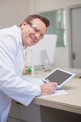 Fototapeta na wymiar Smiling scientist holding tablet writing on notebook