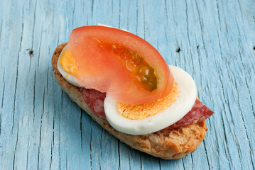Rusk sandwich with salami, egg and tomato on old wooden table