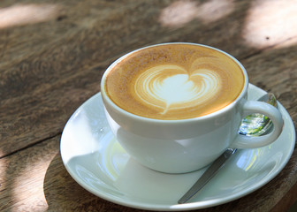 A cup of coffee with heart pattern in a white cup on wooden back