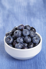 heap of fresh washed blueberries in white bowl on blue wood