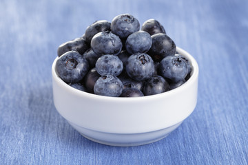 heap of fresh washed blueberries in white bowl on blue wood