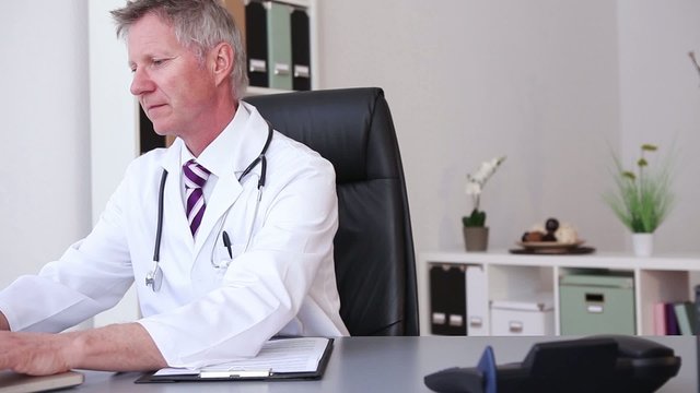 Doctor with stethoscope around his neck working at laptop