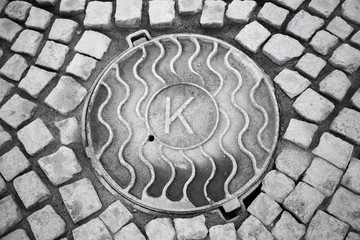 Round hatch in urban stone pavement with K letter